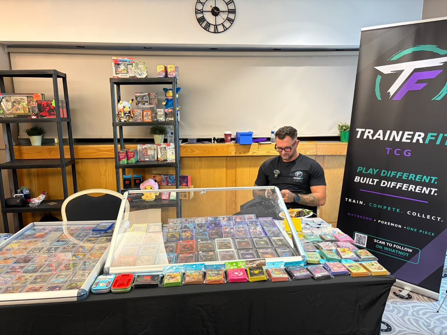 Man sitting behind a table of trading cards at a TrainerFit TCG vendor booth.